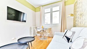 Una sala de estar moderna con un sofá, una mesita redonda, un televisor de pantalla plana en la pared y un comedor con mesa y sillas.