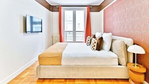 Un dormitorio con cama, televisor montado en la pared, ventana con cortinas y pared con diseño.