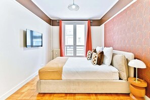 A bedroom with a bed, a TV mounted on the wall, a window with curtains, and a patterned wall. - Charming apartment in Neuilly-sur-Seine (Neuilly-sur-Seine)