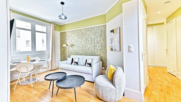 Una sala de estar moderna con un sofá, dos mesas redondas, una zona de comedor con mesa y sillas, y un ventanal grande.