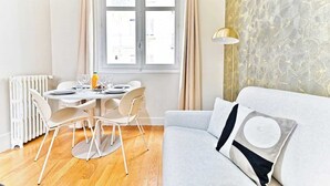 Una sala de estar moderna con un sofá gris, una mesa de comedor con sillas, un radiador y una ventana con cortinas.