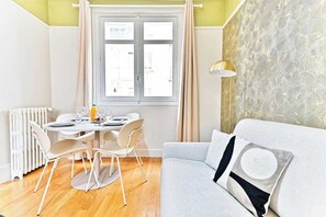 A modern living room with a grey sofa, a dining table with chairs, a radiator, and a window with curtains. - Charming apartment in Neuilly-sur-Seine (Neuilly-sur-Seine)