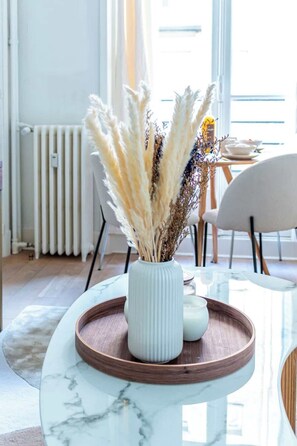 Eine weiße Vase mit getrocknetem Pampasgras und anderen Pflanzen auf einem Marmortisch mit einer Holzschale.