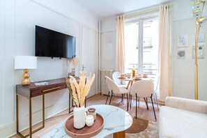 Ein modernes Wohnzimmer mit Flachbildfernseher an der Wand, einem Holztischchen mit Lampe, einem Marmortisch und einem weißen Sofa.