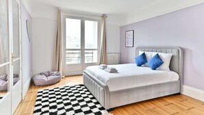A bedroom with a bed, a checkered rug, a pet bed, and a window with curtains. - Superb 2-bedroom apartment in Neuilly-sur-Seine (Neuilly-sur-Seine)