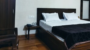 Une chambre à coucher avec un lit en bois, une literie blanche, une petite table de chevet avec un téléphone et des lunettes, et une armoire en bois.