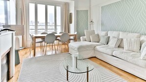 Een moderne woonkamer met een witte bank, een glazen salontafel en een eethoek met stoelen en een tafel.