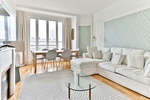 A modern living room with a white sofa, a glass coffee table, and a dining area with chairs and a table. - Beautiful apartment with unobstructed views in Neuilly (Neuilly-sur-Seine)