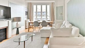 Een moderne woonkamer met een bank, een glazen salontafel, een televisie en een eethoek met stoelen en een tafel.