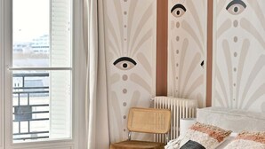 Een slaapkamer met een groot bed, een rieten stoel, een radiator en een raam met gordijnen.