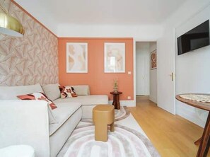 A modern living room with a sofa, a small stool, and a round table. There are two framed artworks on the wall. - An intimate and bright haven in Neuilly (Neuilly-sur-Seine)