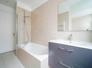 A modern bathroom with a glass shower enclosure, a white bathtub, and a grey vanity with a mirror. - An intimate and bright haven in Neuilly (Neuilly-sur-Seine)