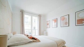 A bedroom with a bed, a window with curtains, and framed pictures on the wall. - An intimate and bright haven in Neuilly (Neuilly-sur-Seine)