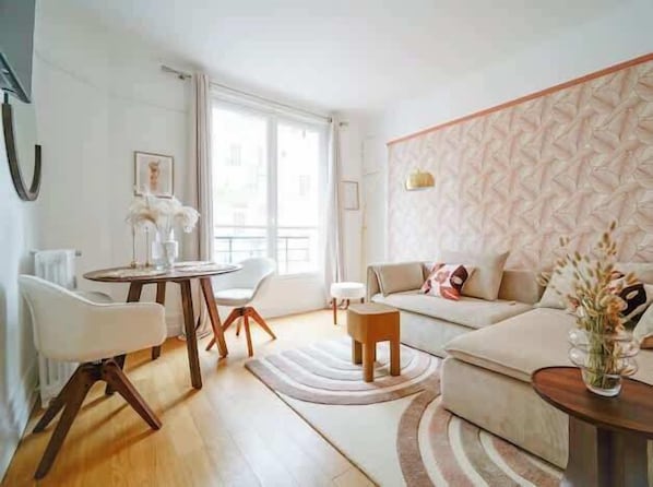 A modern living room with a round wooden table, white chairs, a beige sofa, and a patterned wall. - An intimate and bright haven in Neuilly (Neuilly-sur-Seine)
