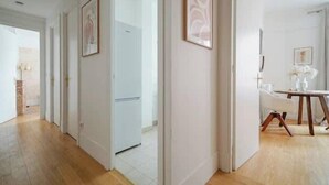 A hallway with wooden flooring, white walls, and doors leading to rooms. There are framed pictures on the walls and a dining area with a table and chairs. - An intimate and bright haven in Neuilly (Neuilly-sur-Seine)