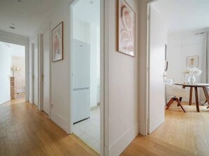 A hallway with wooden flooring, white walls, and doors leading to rooms. There are framed pictures on the walls and a dining area with a table and chairs. - An intimate and bright haven in Neuilly (Neuilly-sur-Seine)