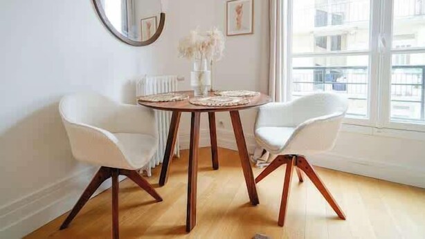 A dining area with a round table, two white chairs, a mirror, and a window with a view of buildings. - An intimate and bright haven in Neuilly (Neuilly-sur-Seine)