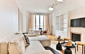 A modern living room with a sofa, a dining table with chairs, a fireplace, and a TV mounted on the wall. - Neuilly-sur-Seine, family cocoon (Neuilly-sur-Seine)
