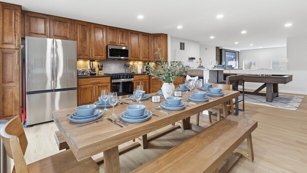 A modern kitchen with wooden cabinets, stainless steel appliances, and a dining area set for six with blue tableware. - Amazing 5BR Retreat Near Downtown Indy (Indianapolis)