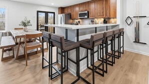A modern kitchen with wooden cabinets, a central island with bar stools, and a dining area with a table and chairs. - Amazing 5BR Retreat Near Downtown Indy (Indianapolis)