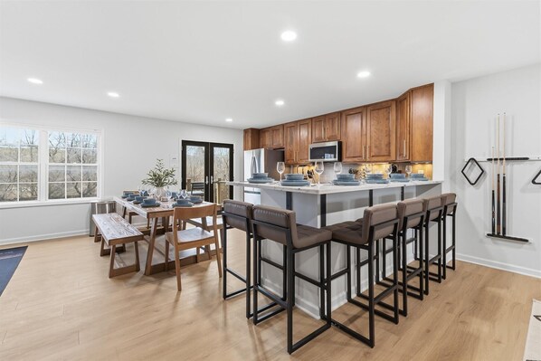 Una cocina moderna con armarios de madera, una isla central con taburetes y una zona de comedor con mesa y sillas.