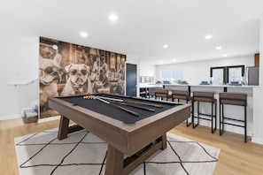Una sala de estar moderna con mesa de billar, un cuadro abstracto grande y una zona de bar con taburetes.