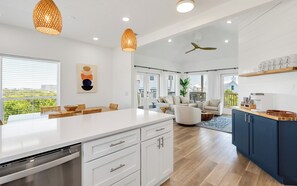 Una cocina moderna con una isla grande, armarios blancos y vistas al exterior.