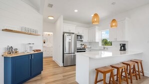 A modern kitchen with white cabinetry, a stainless steel refrigerator, wooden stools, and pendant lighting. - Mystic Hideaway 7 BR + Private Pool & Pet Friendly (Inlet Beach)