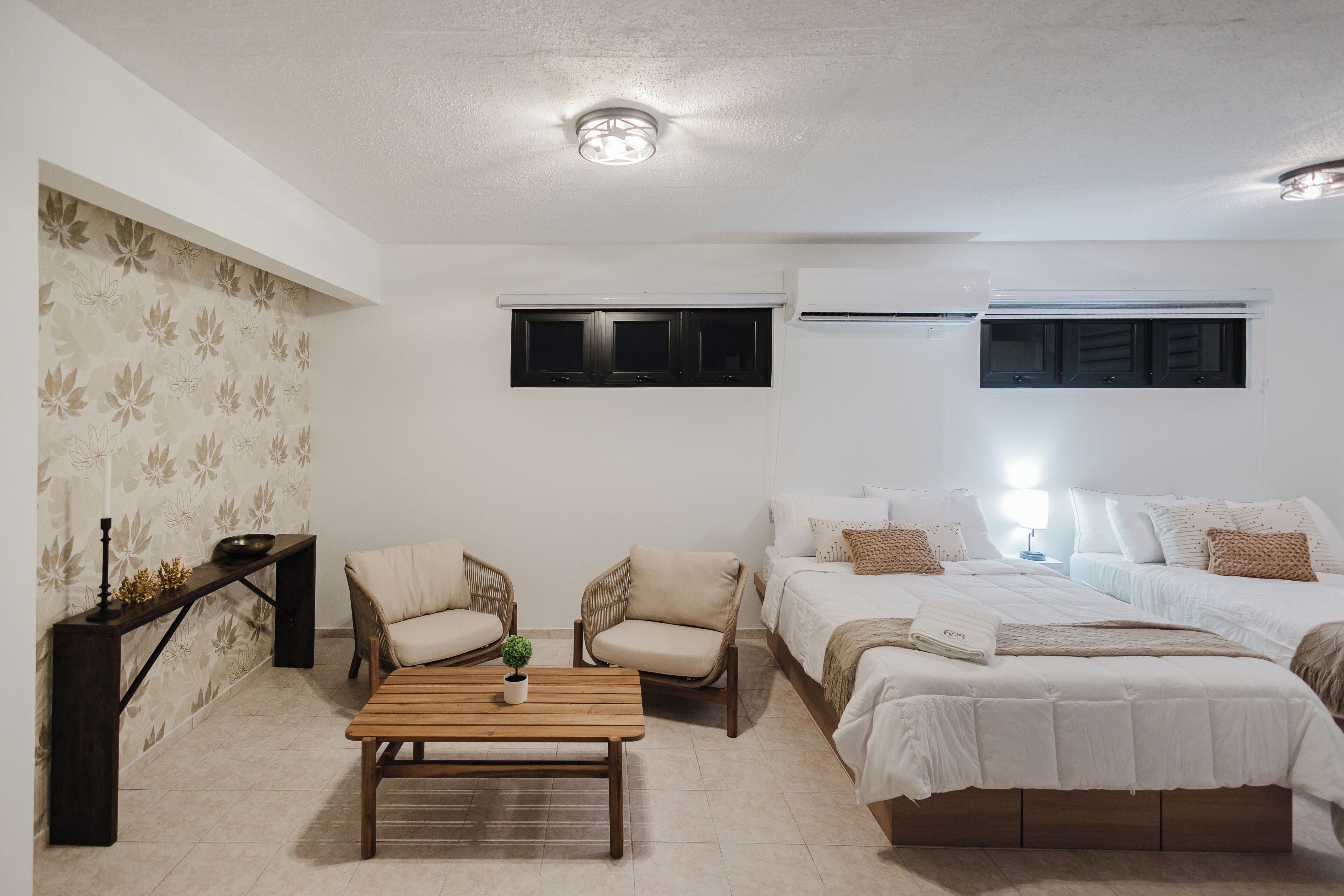 A bedroom with a bed, two chairs, a table, and an air conditioning unit.