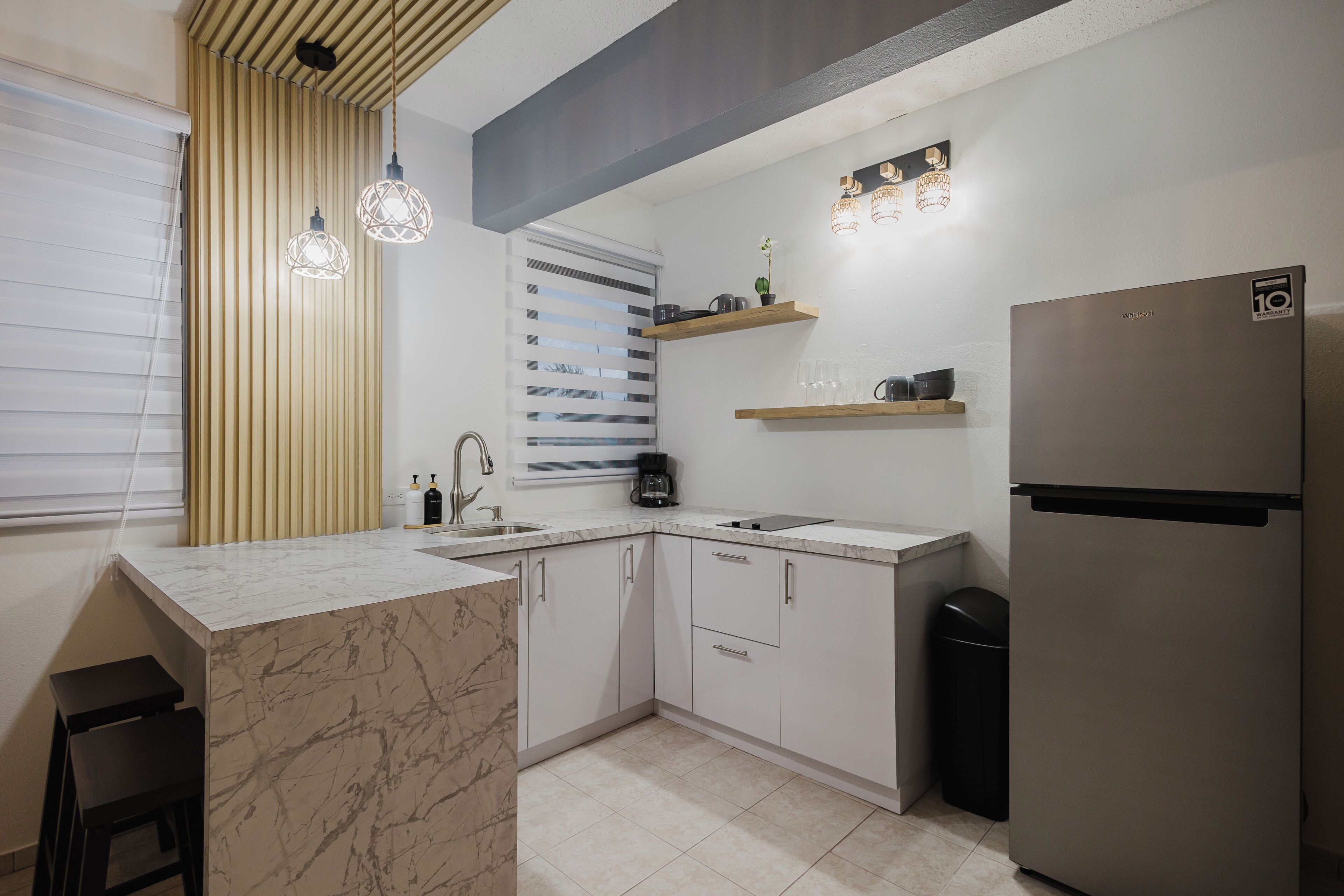 A modern kitchen with a marble countertop, stainless steel appliances, and pendant lighting.