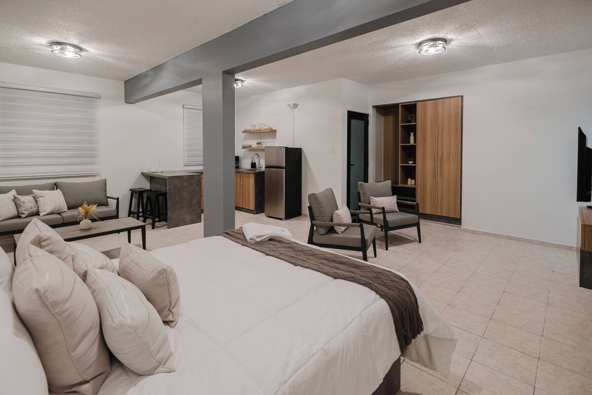 A modern hotel room with a large bed, a sofa, a dining area, and a TV.