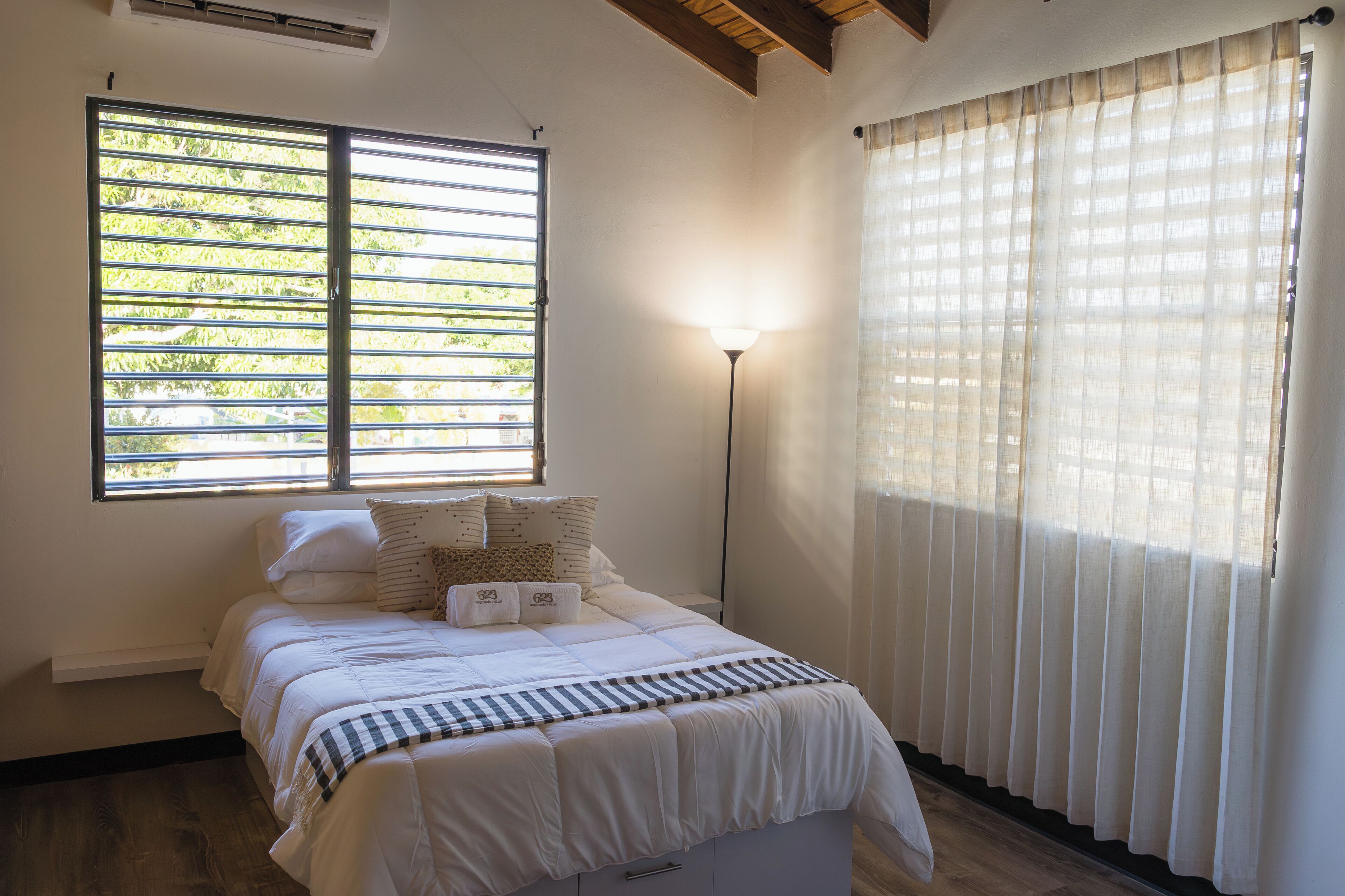 A bedroom with a bed, a window with blinds, a standing lamp, and a curtain.