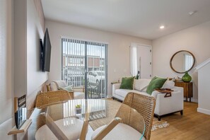 A modern living room with a glass dining table, wicker chairs, a white sofa with green cushions, and a large window with a view of the street. - 3 Suites lovely Home Minutes from Disney Area 3216 (Kissimmee)