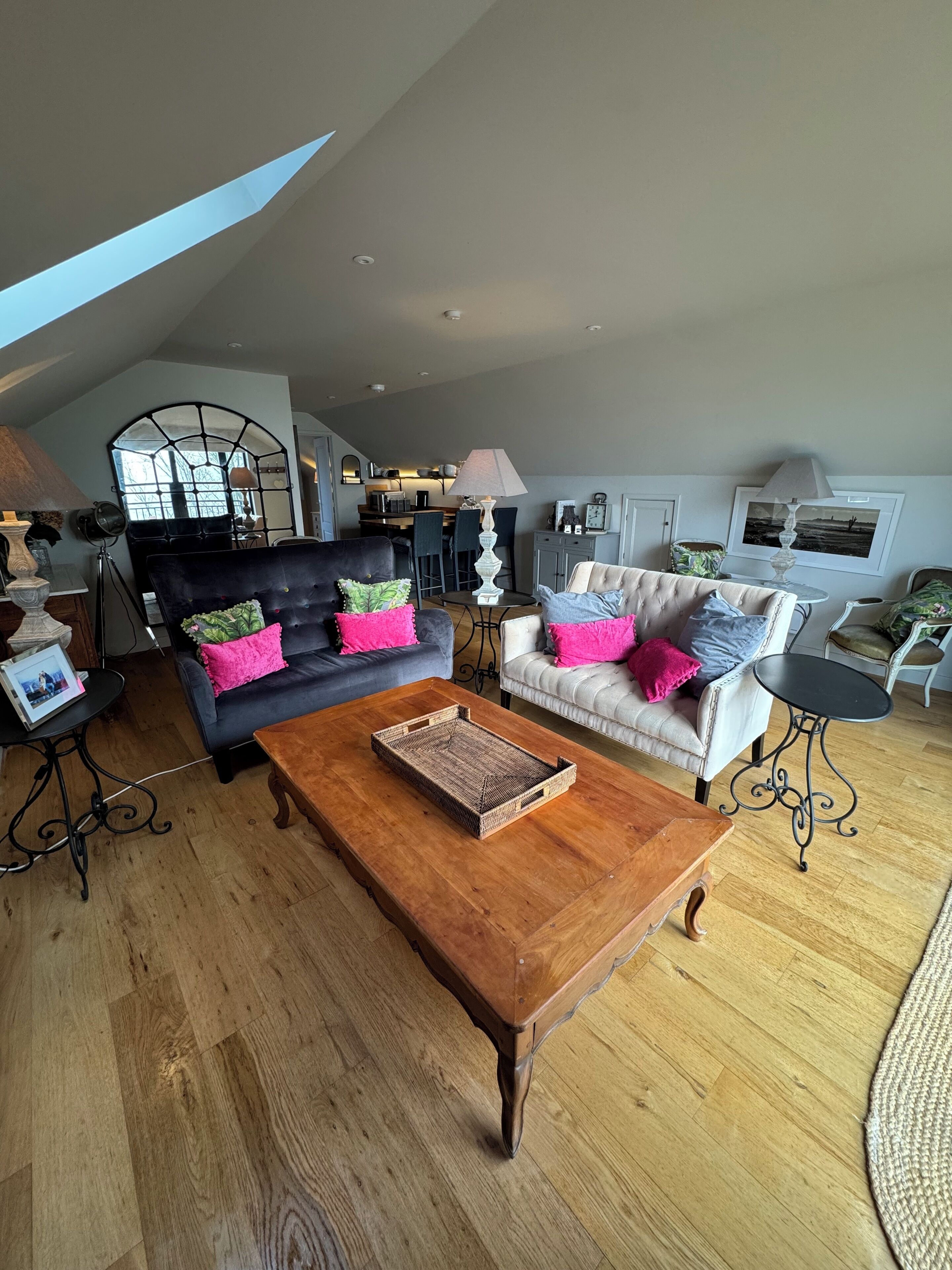 A spacious living room with a high ceiling, a wooden coffee table, and two sofas with colorful cushions.