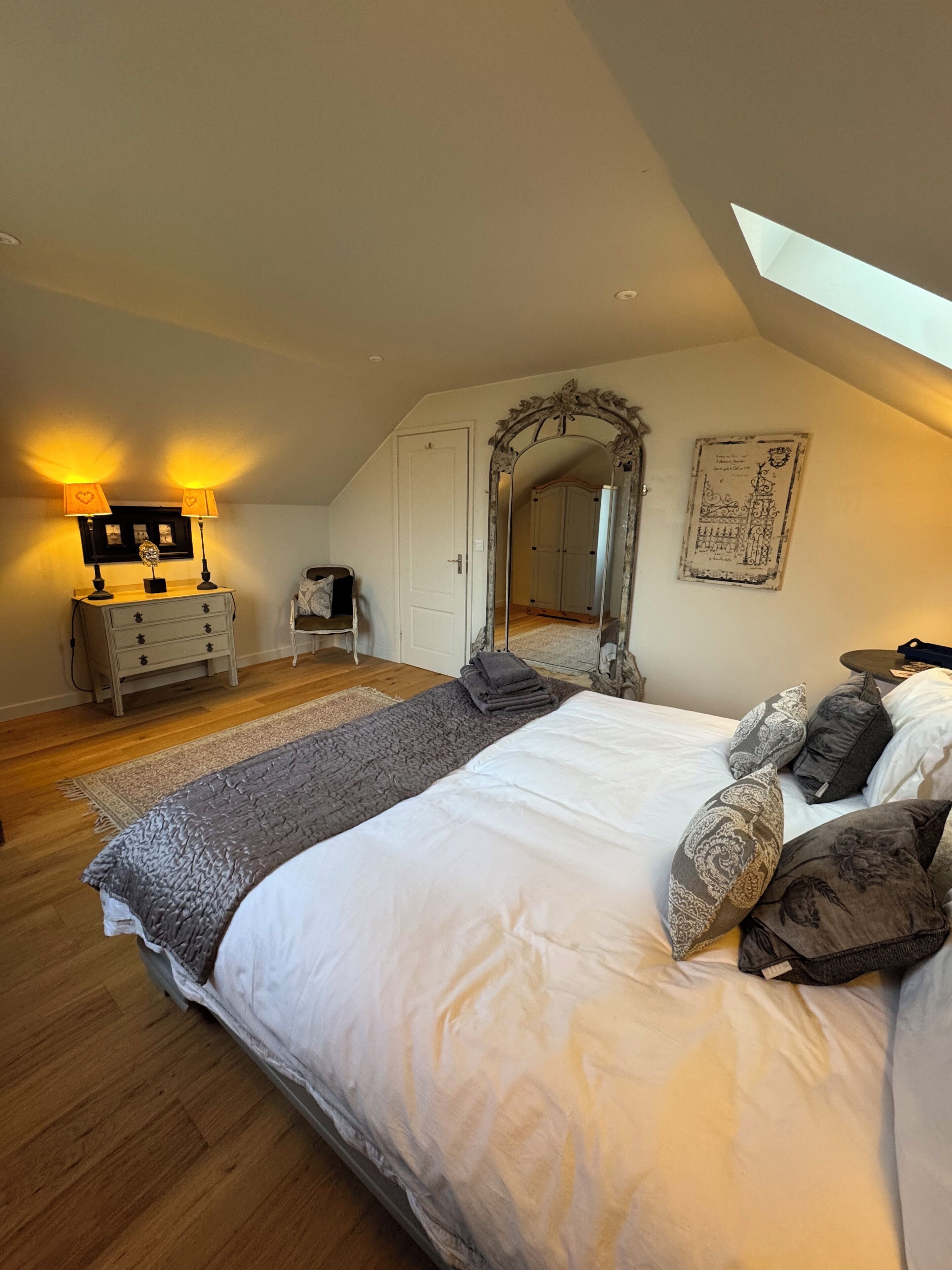 Une chambre à coucher avec un grand lit, un miroir, une commode et une table de chevet.