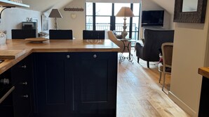 A modern kitchen with a dark island, wooden flooring, and a dining area with a TV and seating.