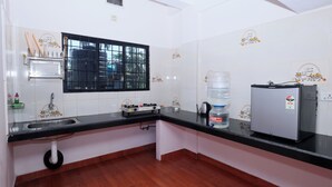 Una cocina con encimera negra, azulejos blancos, ventana con reja negra, dispensador de agua y refrigerador.