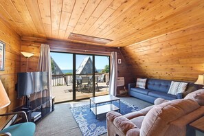 Interior de madera con televisor, sofá y vistas al exterior.