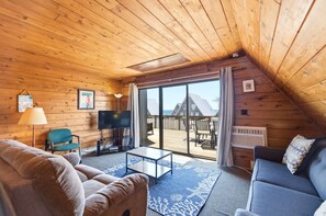 Interior acogedor de una cabaña con paredes de madera, un sofá, una mesa y un televisor.