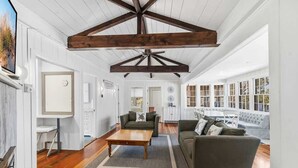 Een ruime woonkamer met houten vloeren, een groot balken plafond en uitzicht op buiten.