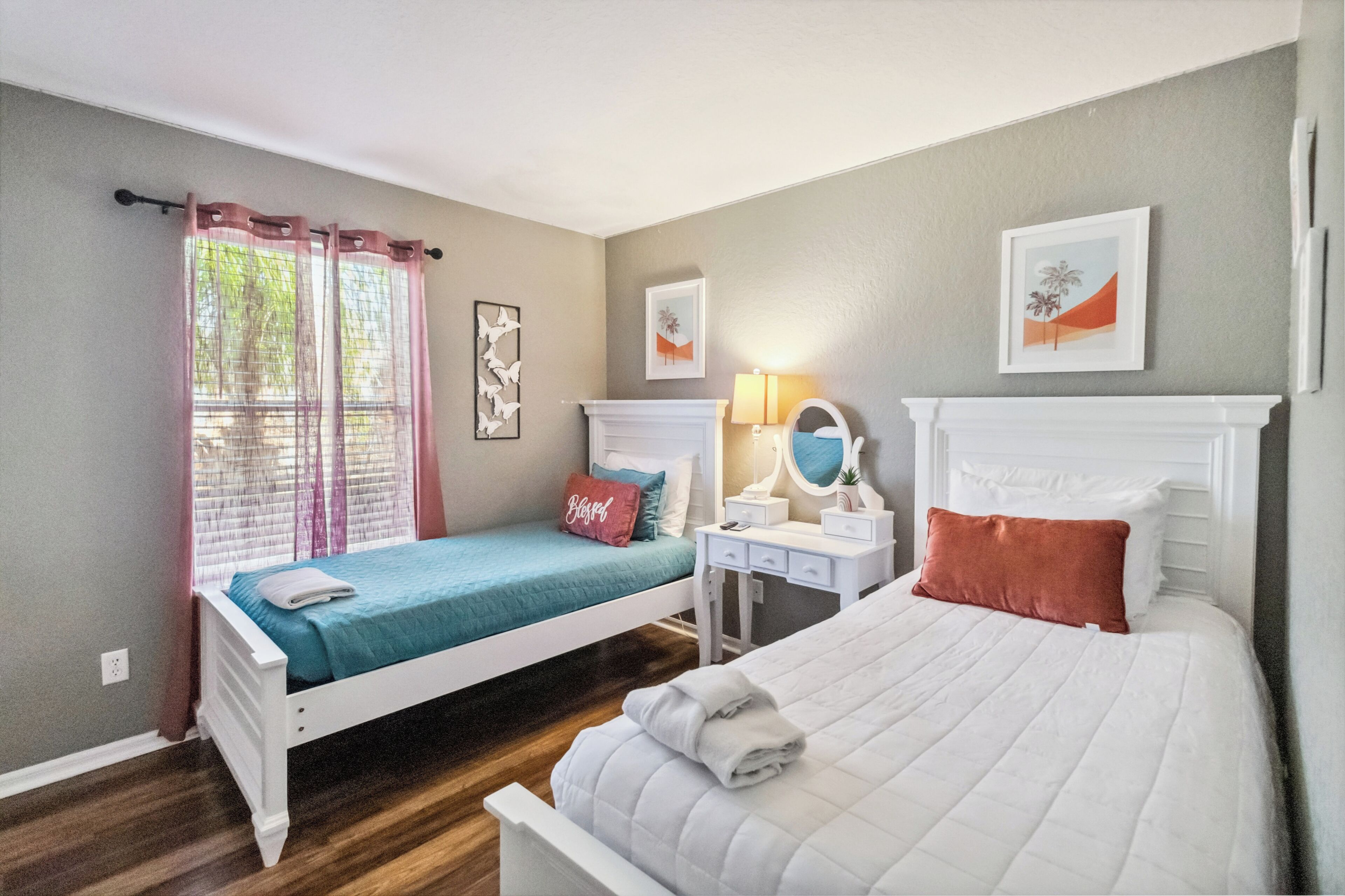 A bedroom with two beds, a vanity with a mirror, and artwork on the walls.