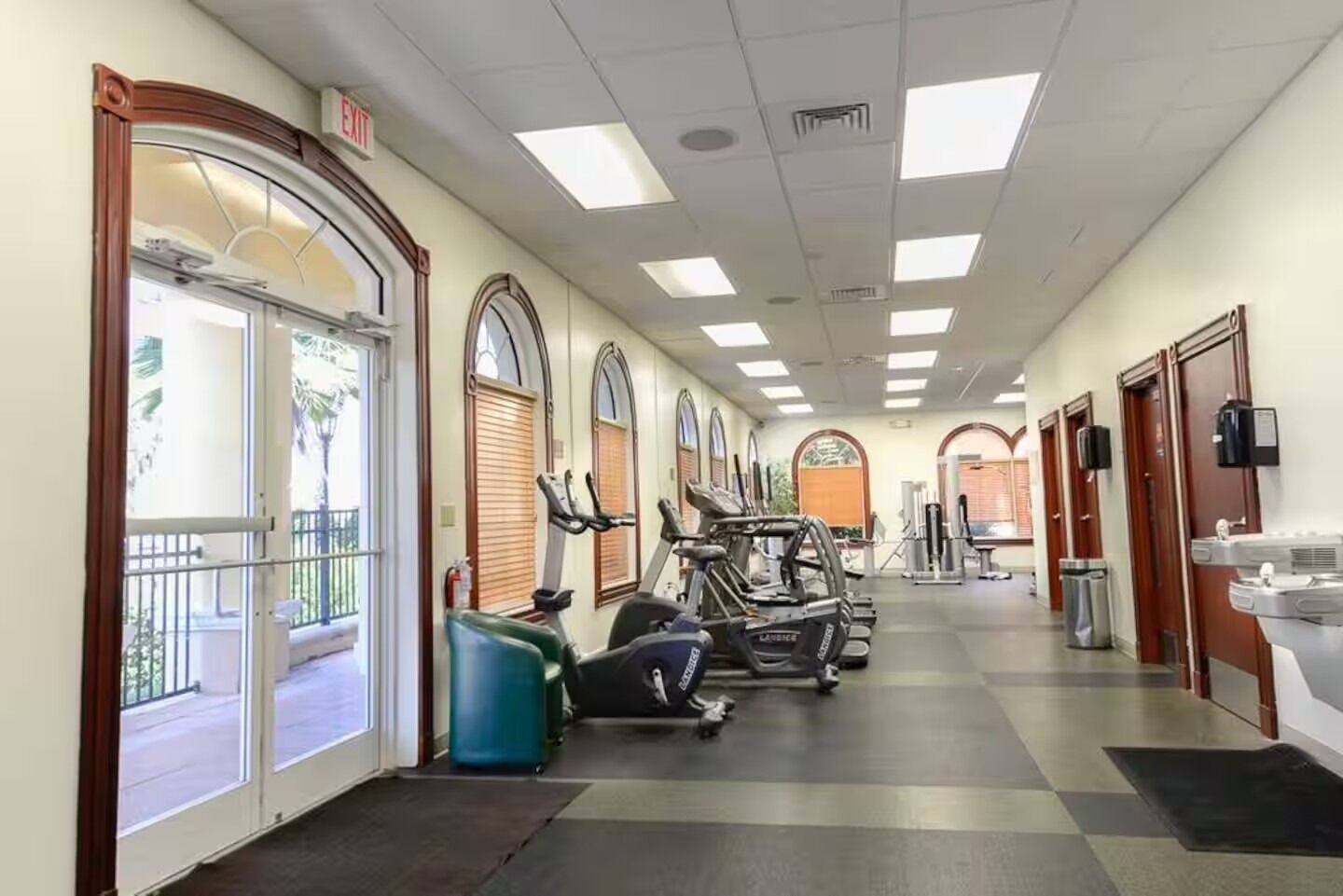 A gym with exercise equipment, a water fountain, and a trash can.