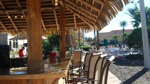 A covered outdoor seating area with wooden furniture and a thatched roof. - Near Disney Family Fun with Resort pools, Lazy River, Arcade, Restaurants (Davenport)
