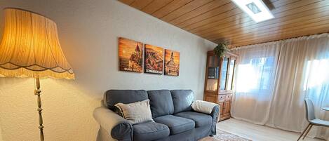 A living room with a sofa, a lamp, a wooden chest, and wall art.