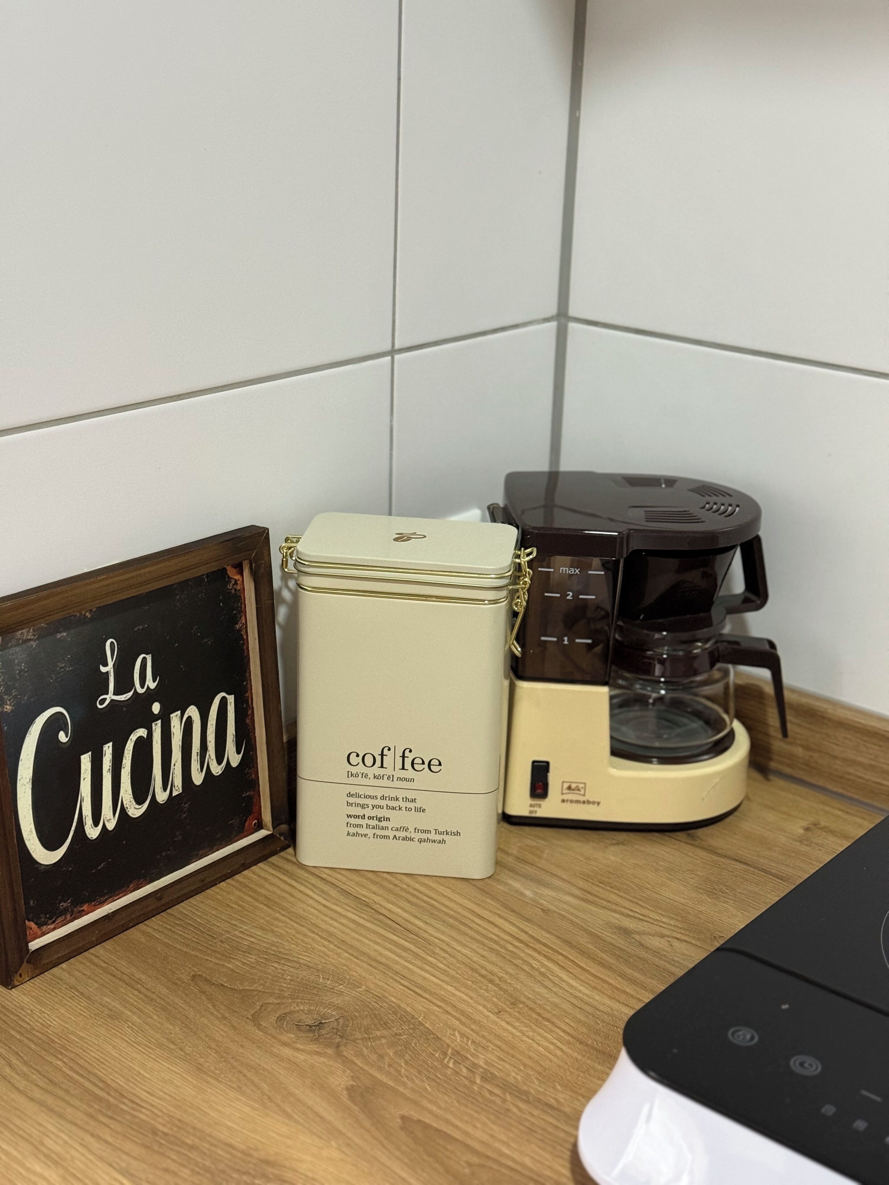 A kitchen counter with a coffee maker, a framed sign reading 'La Cucina,' and a container labeled 'coffee.'