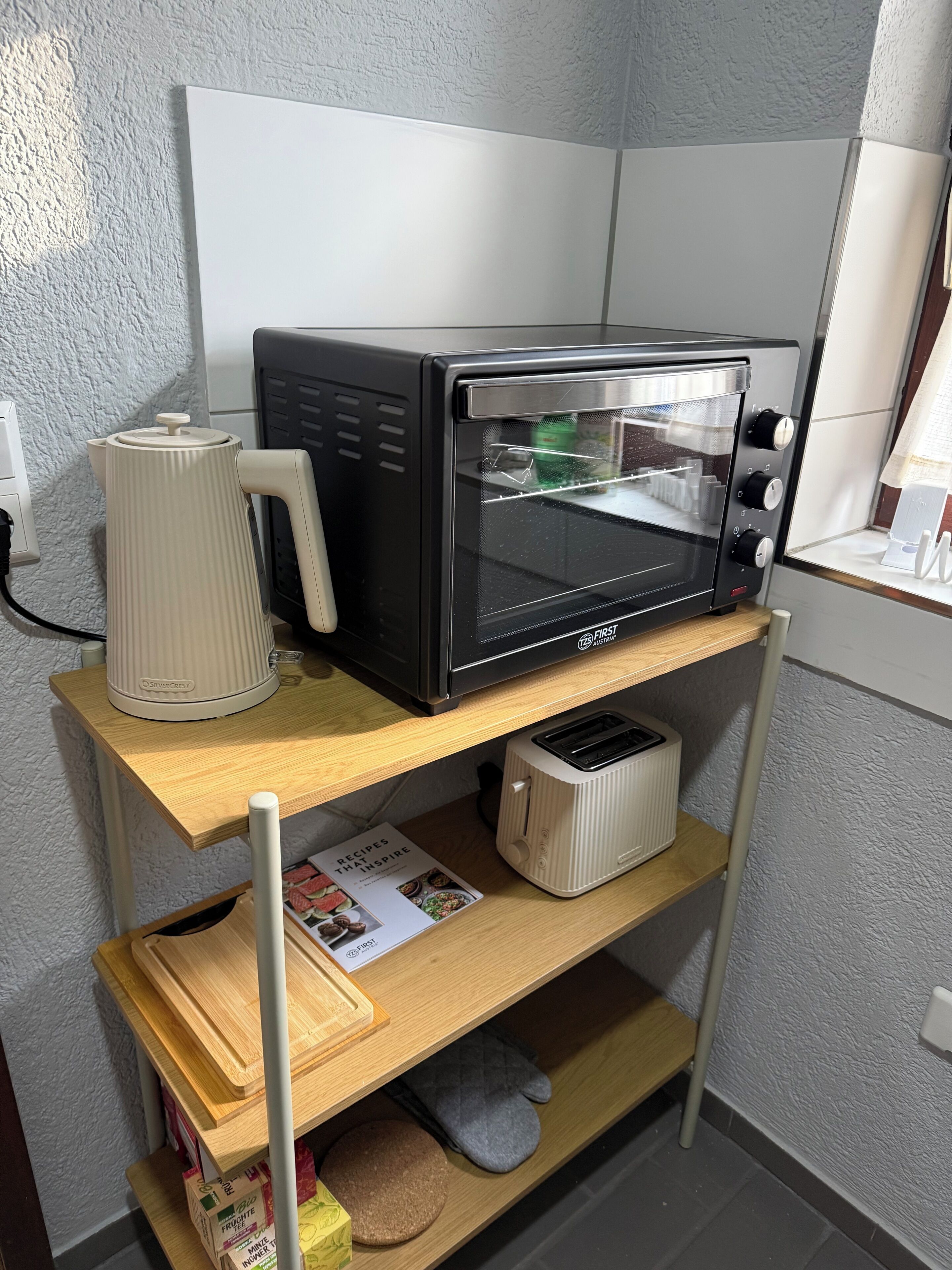 Een keuken met een zwart toaster op een houten plank, een witte waterkoker en een kookboek getiteld 'Recipes That Inspire'.