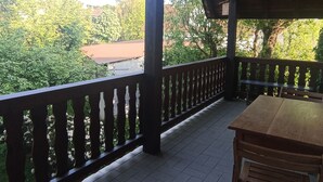 En overdækket balkon med et træbord og stole, med udsigt over en have og bygninger.