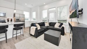A modern kitchen with white cabinets, a stainless steel refrigerator, and a bar area with two black bar stools. - Modern 2BR Townhome Near NRG • Med Center • Downtown w/ Garage (Houston)
