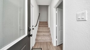 A hallway with a carpeted staircase, white walls, and a door with a window. - Modern 2BR Townhome Near NRG • Med Center • Downtown w/ Garage (Houston)