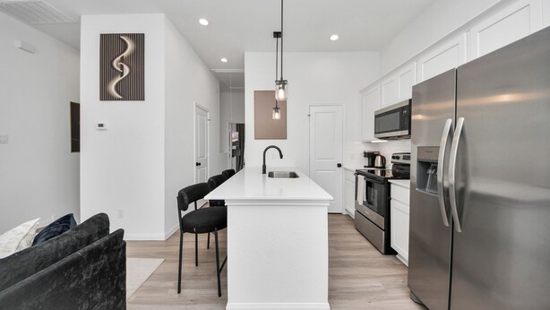 A modern kitchen with white cabinetry, a central island, stainless steel appliances, and a pendant light. - Modern 2BR Townhome Near NRG • Med Center • Downtown w/ Garage (Houston)
